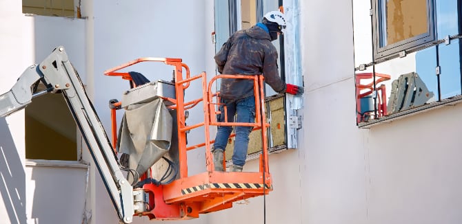 Painter in lifting platform at height caulking around building windows.